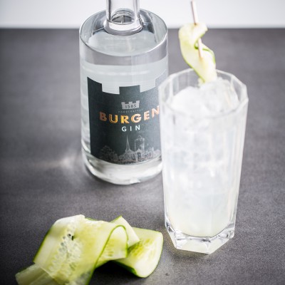 Flasche des Burgen Gin, ein Glas mit dem Burgen Gin und Gurke